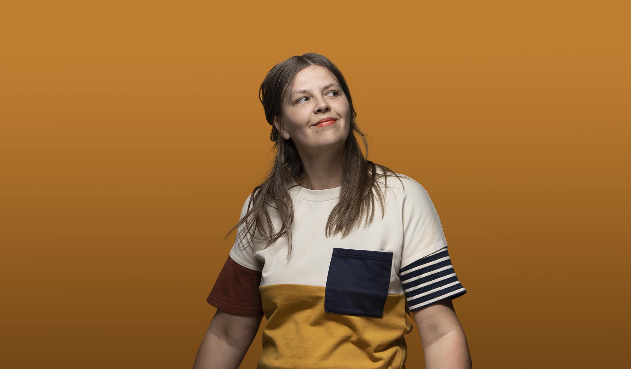 a woman in a striped t - shirt standing in front of an orange background.