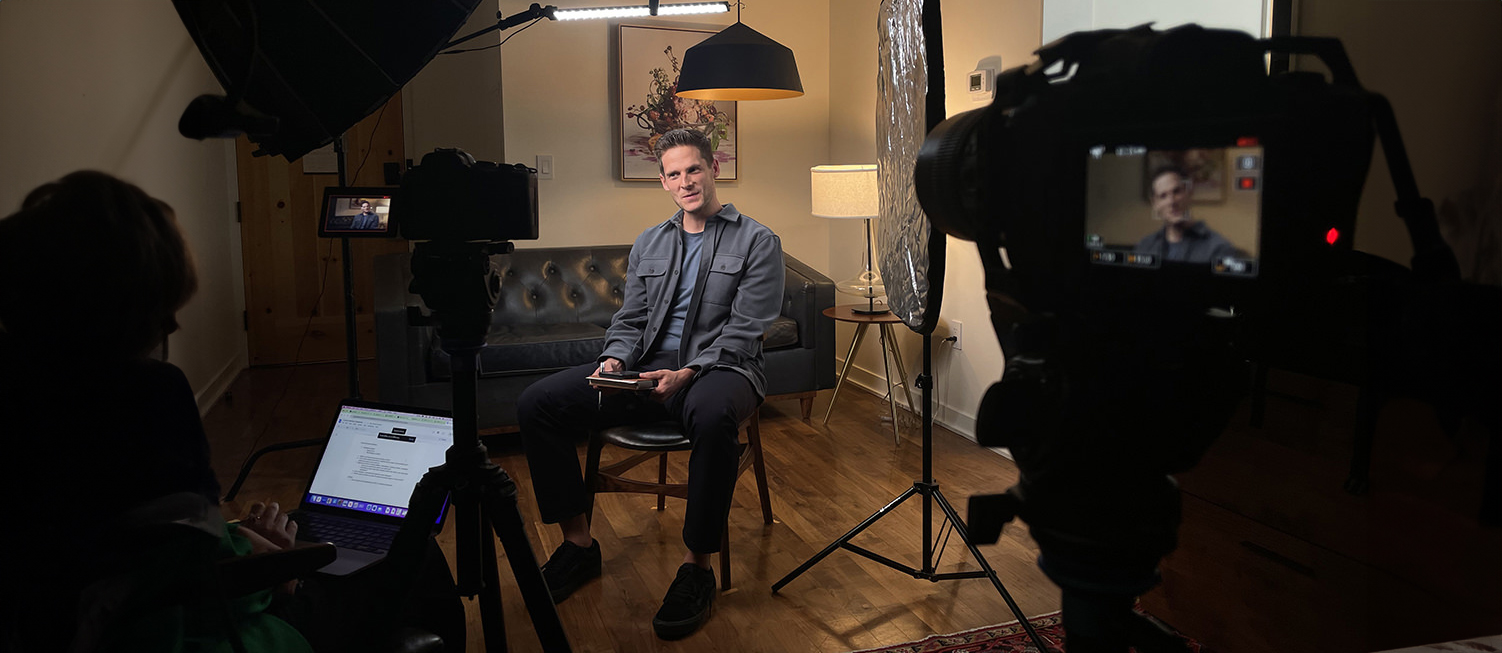 Amidst the glow of lights and the whir of cameras, a person sits poised in a chair, laptop on standby for navigation through the interview's flow.