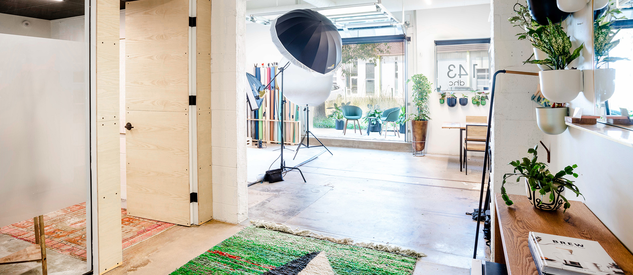 A bright studio with photography equipment, plants, a wooden bench, and a rug. The glass door marked 43 serves as the main navigation to an outdoor patio with seating.