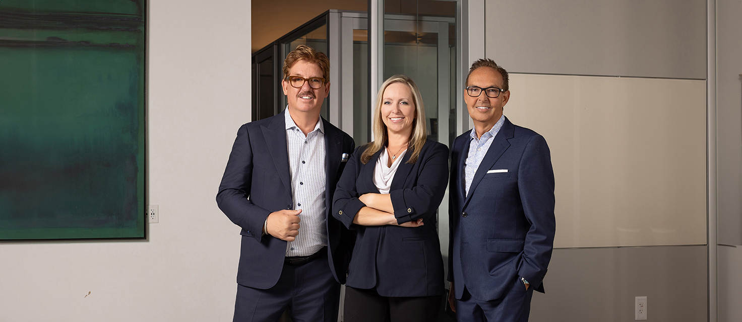 Three people in business attire stand together in an office setting, smiling at the camera, as if they've just mapped out the main navigation for their latest project.