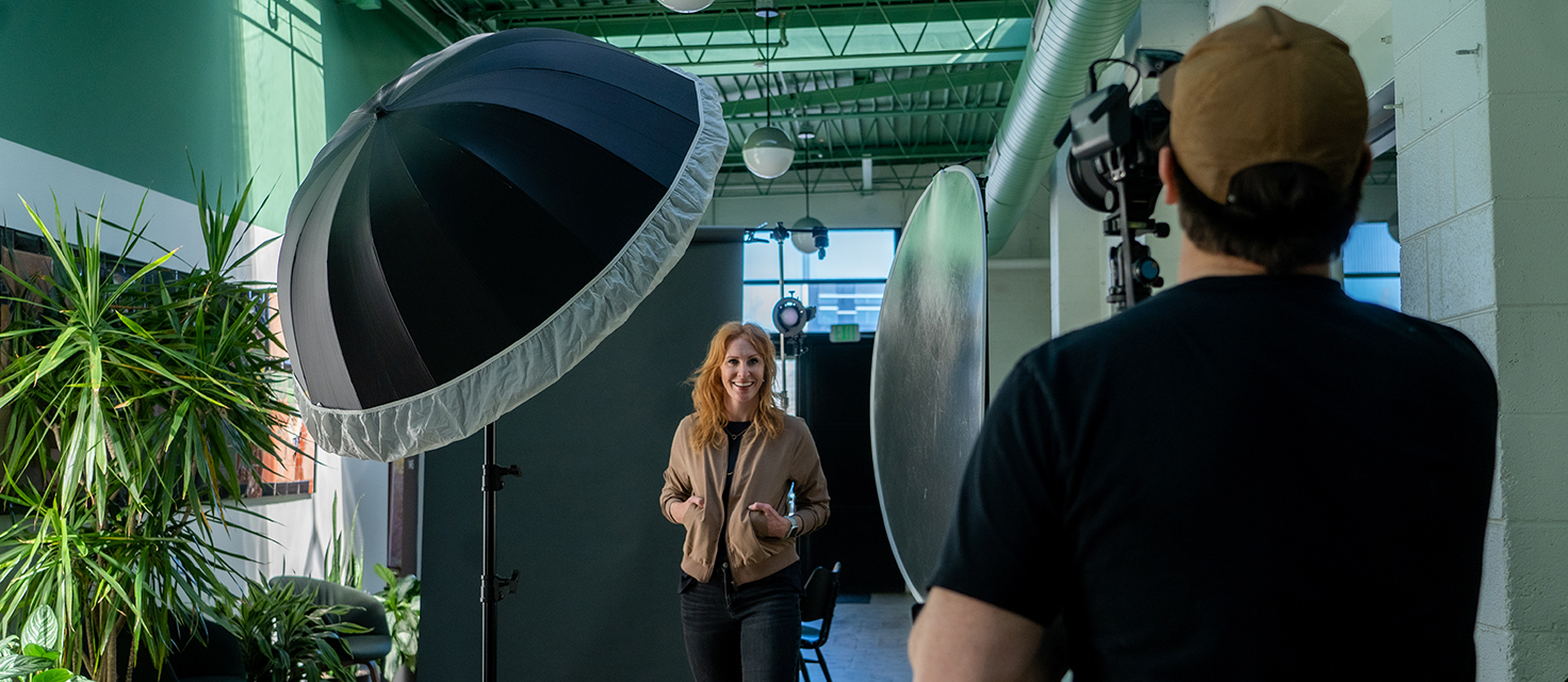 In a studio setting, beneath the glow of a large umbrella light, a person is expertly photographed as they navigate their poses with main aplomb.