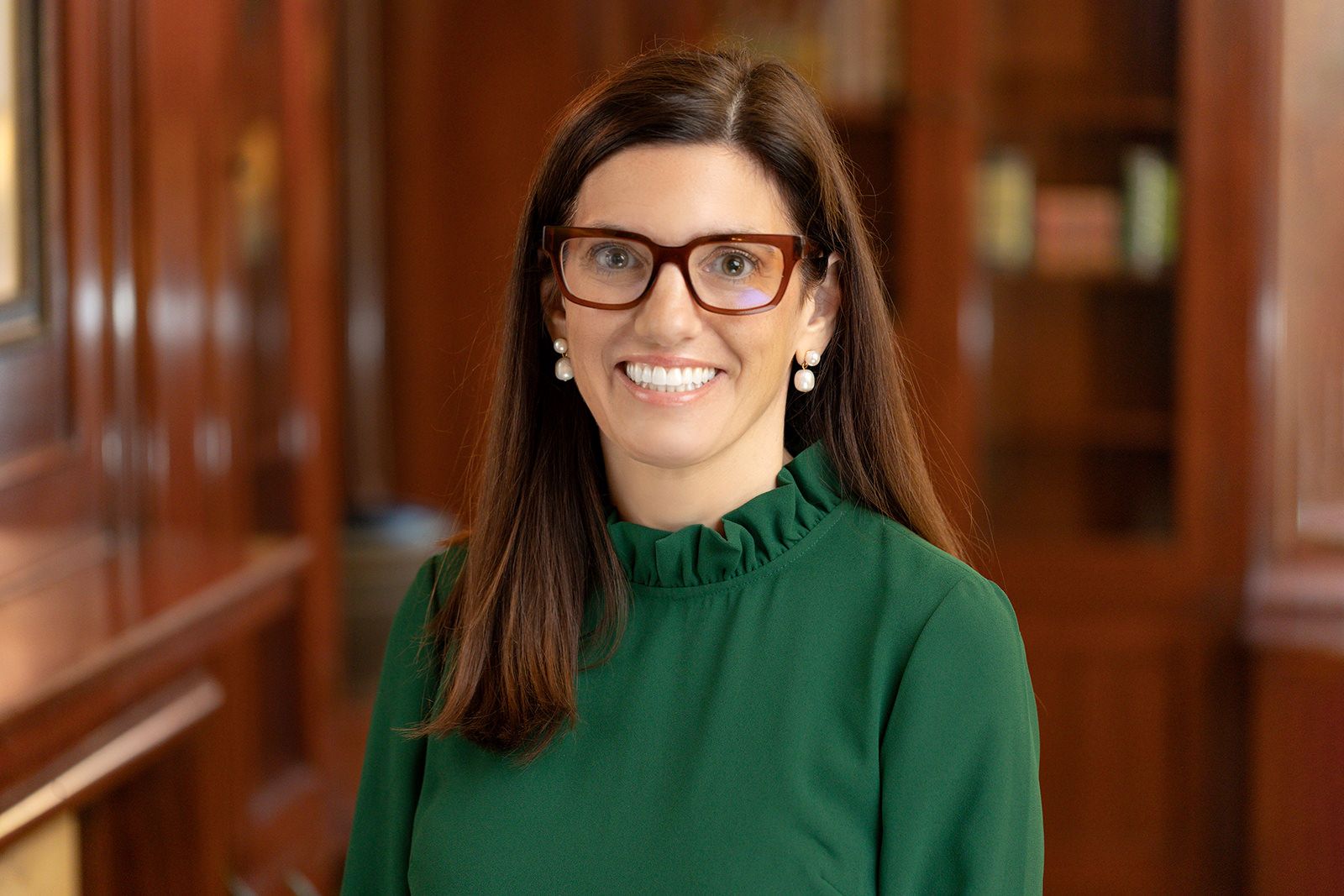 A woman in glasses is smiling in a professional green top for corporate headshots.