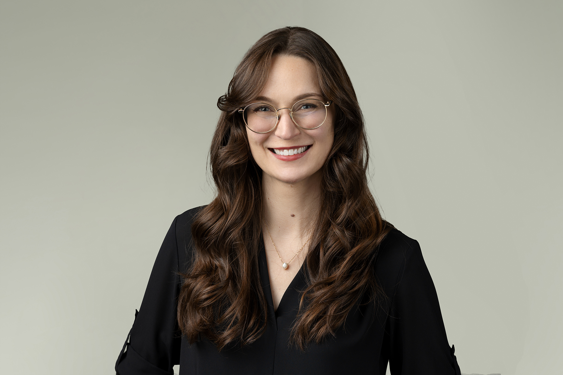 A woman with long curly hair and glasses smiling at the camera against a light background in her Denver headshot.