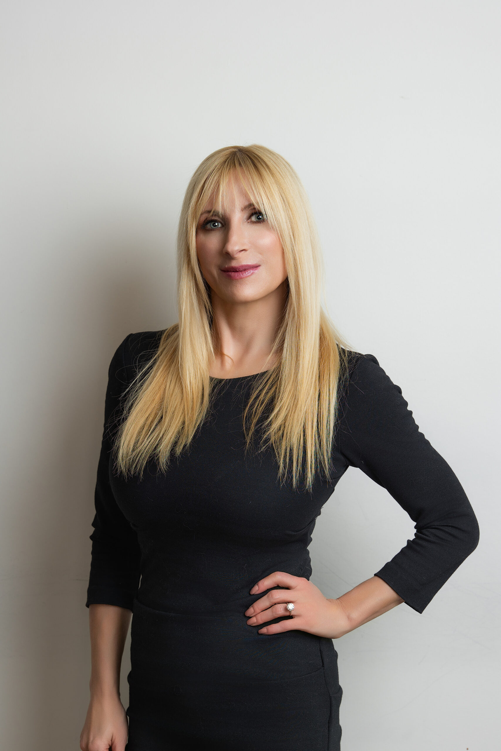 Woman with blonde hair wearing a black dress posing for Denver headshots against a white background.