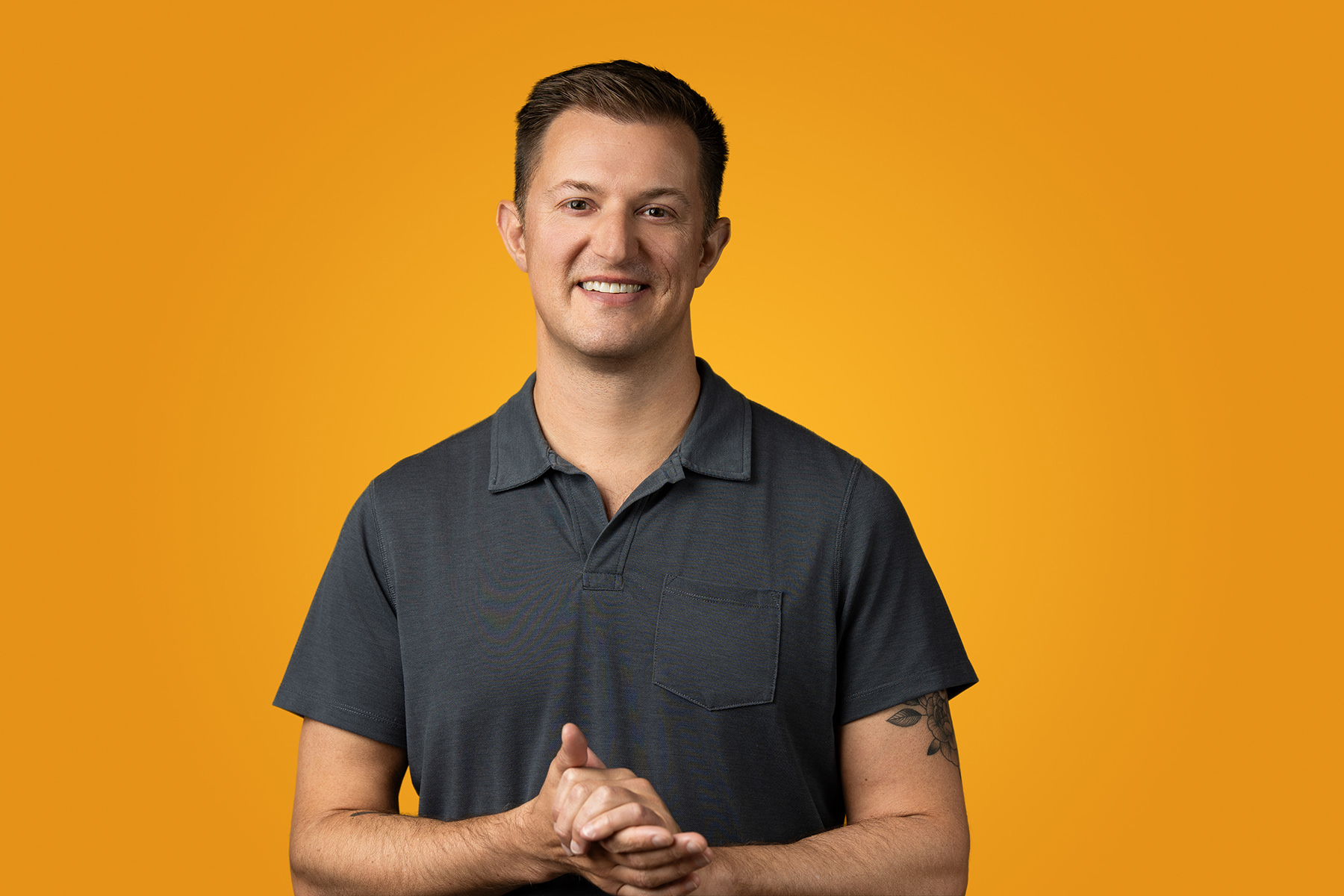 A person smiling in a gray shirt poses for a headshot against an orange background, perfect for their portfolio.