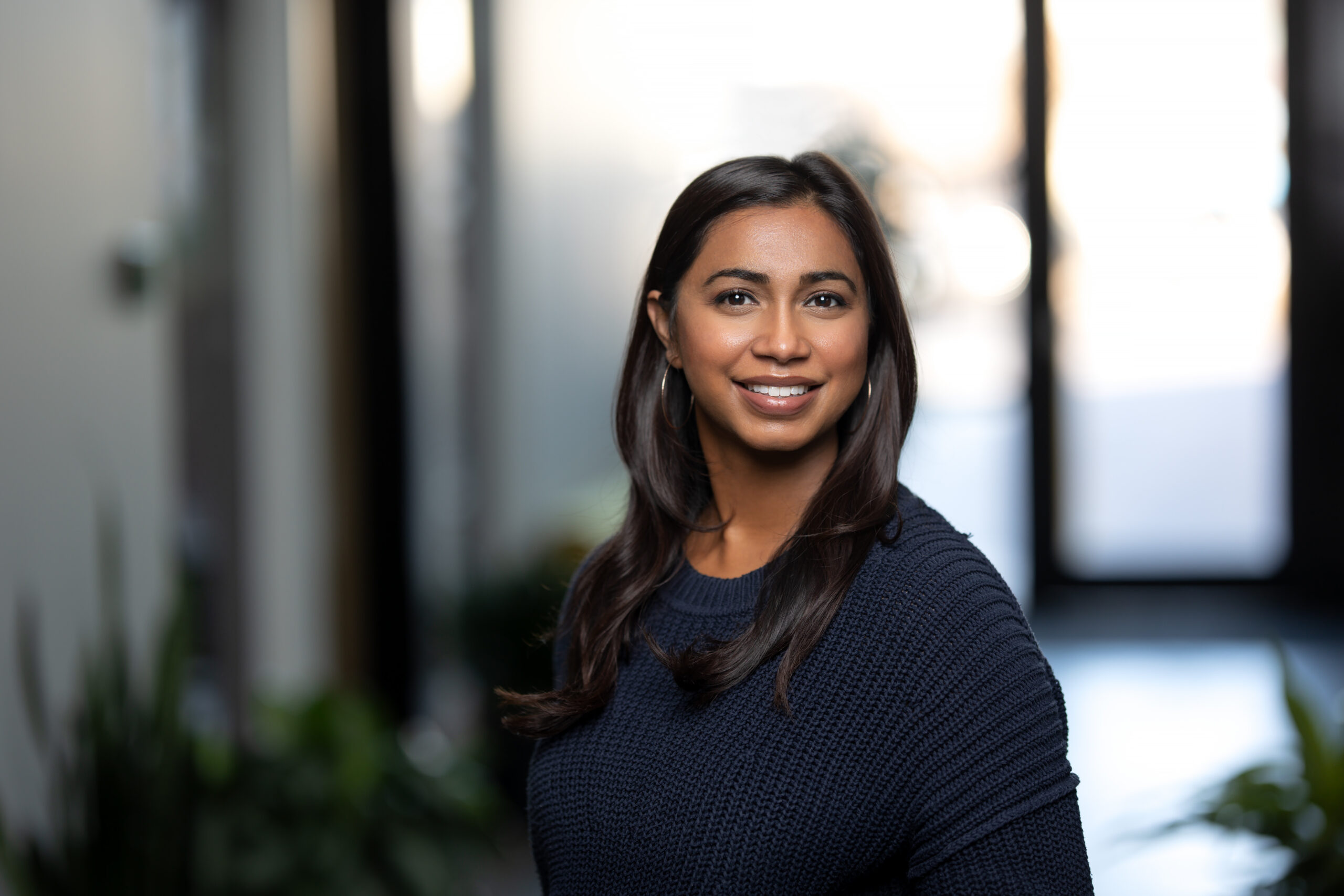 Headshot of a woman in a navy sweater, smiling warmly while standing indoors against a softly blurred background—perfect for any portfolio.