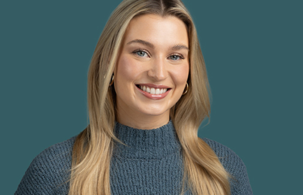 Smiling person with long blonde hair wearing a blue sweater, capturing the essence of company culture against a teal background.