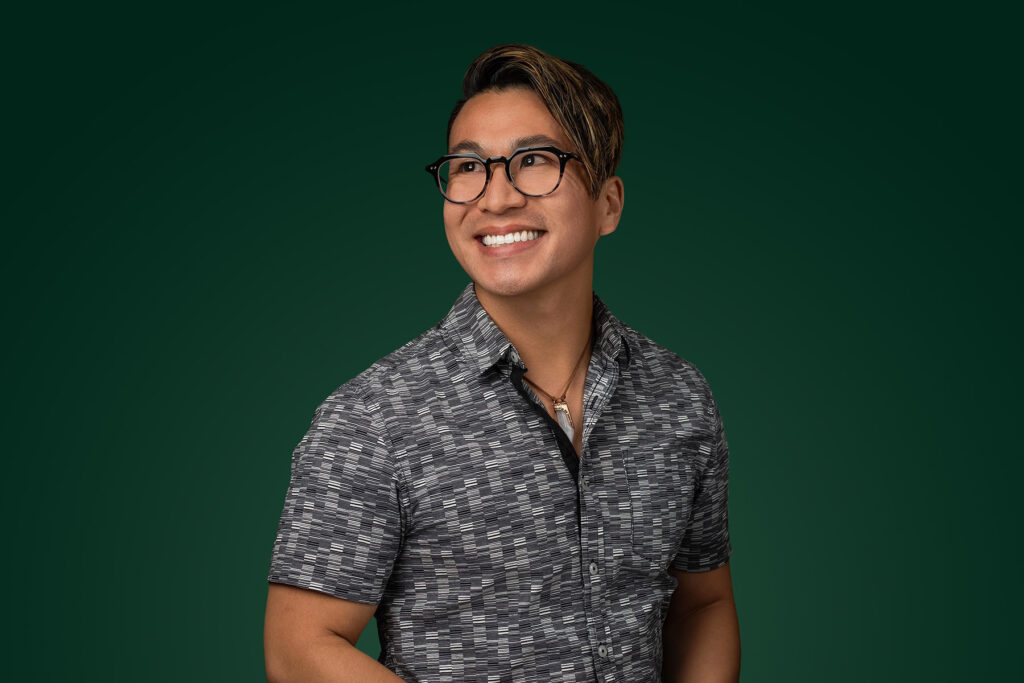 A person with short hair and glasses is smiling while looking to the side, embodying the vibrant spirit of Visual Content trends. They wear a patterned short-sleeve shirt against a dark green background, capturing the innovative essence of Marketing 2025.